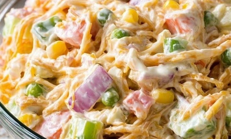 Creamy ranch chicken salad with shredded chicken, cheddar cheese, corn, peas, celery, tomatoes, and red onion in a glass bowl